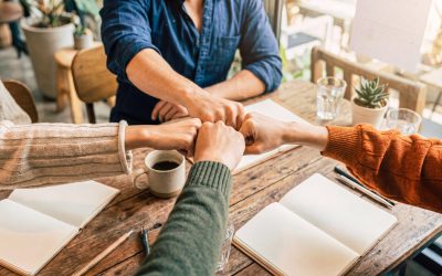 Photograph of diverse team members doing a fist bump over a wooden desk, symbolizing collaboration and unity.